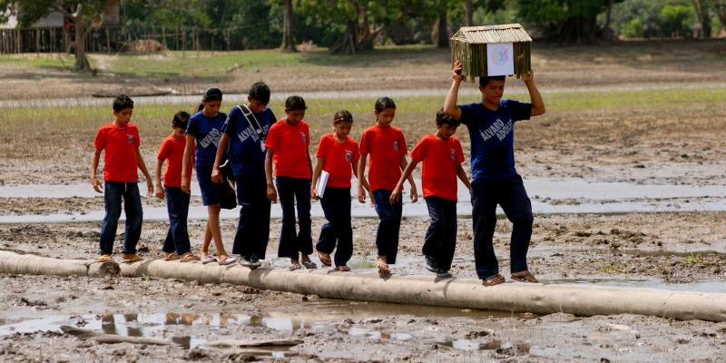 a group of people with a ballot box walking through mud.