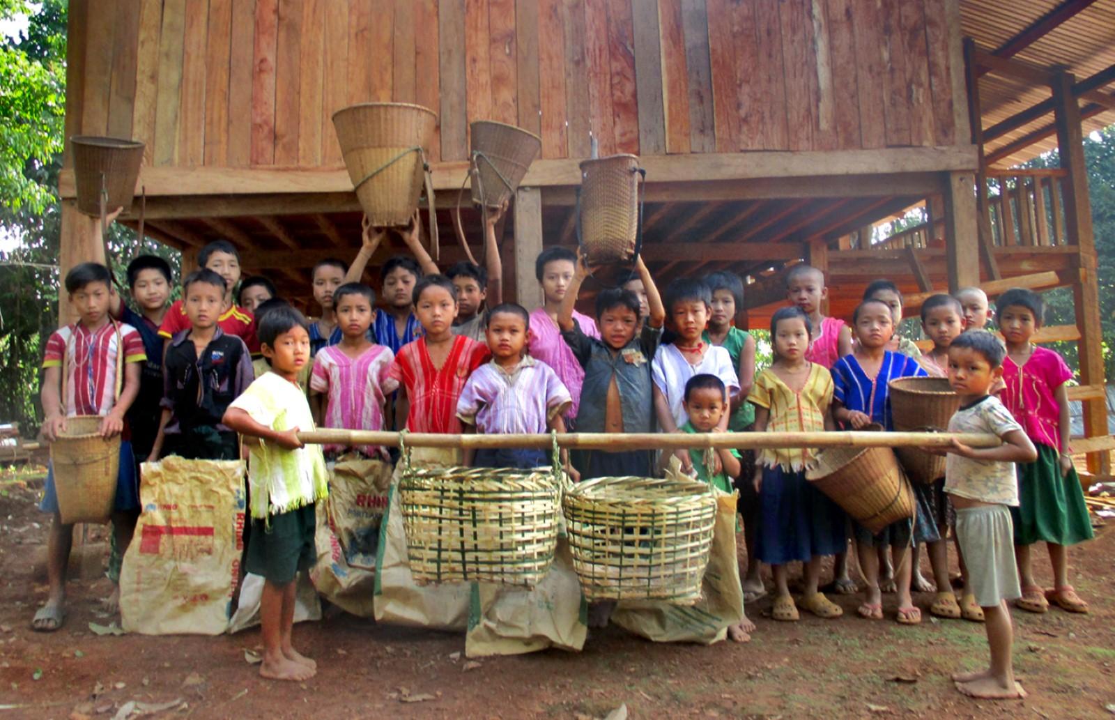Children standing in front of a house, holding bags and buckets, looking into the camera