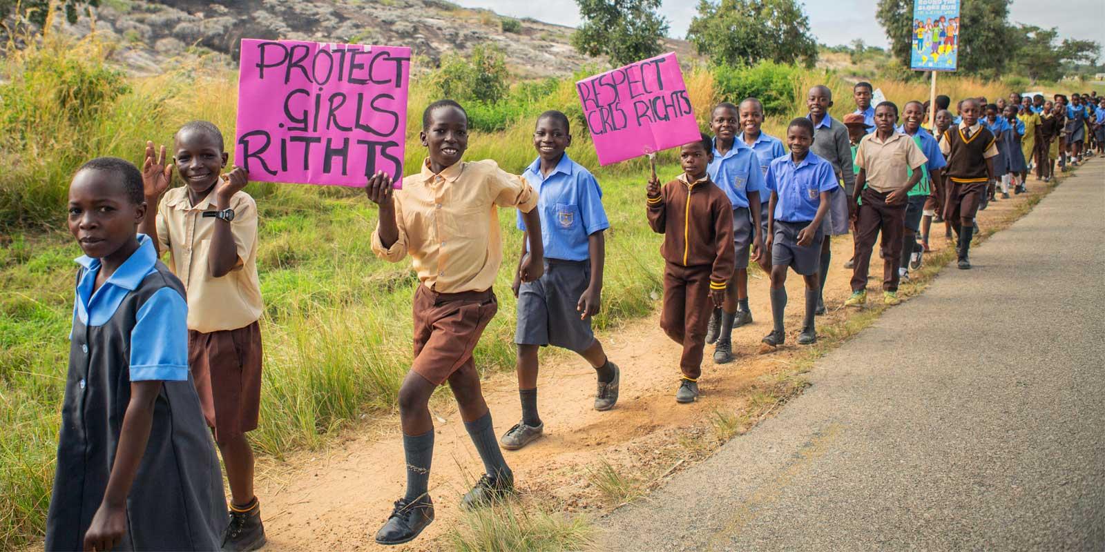 Boys walking with signs along highway in dry African landscape.