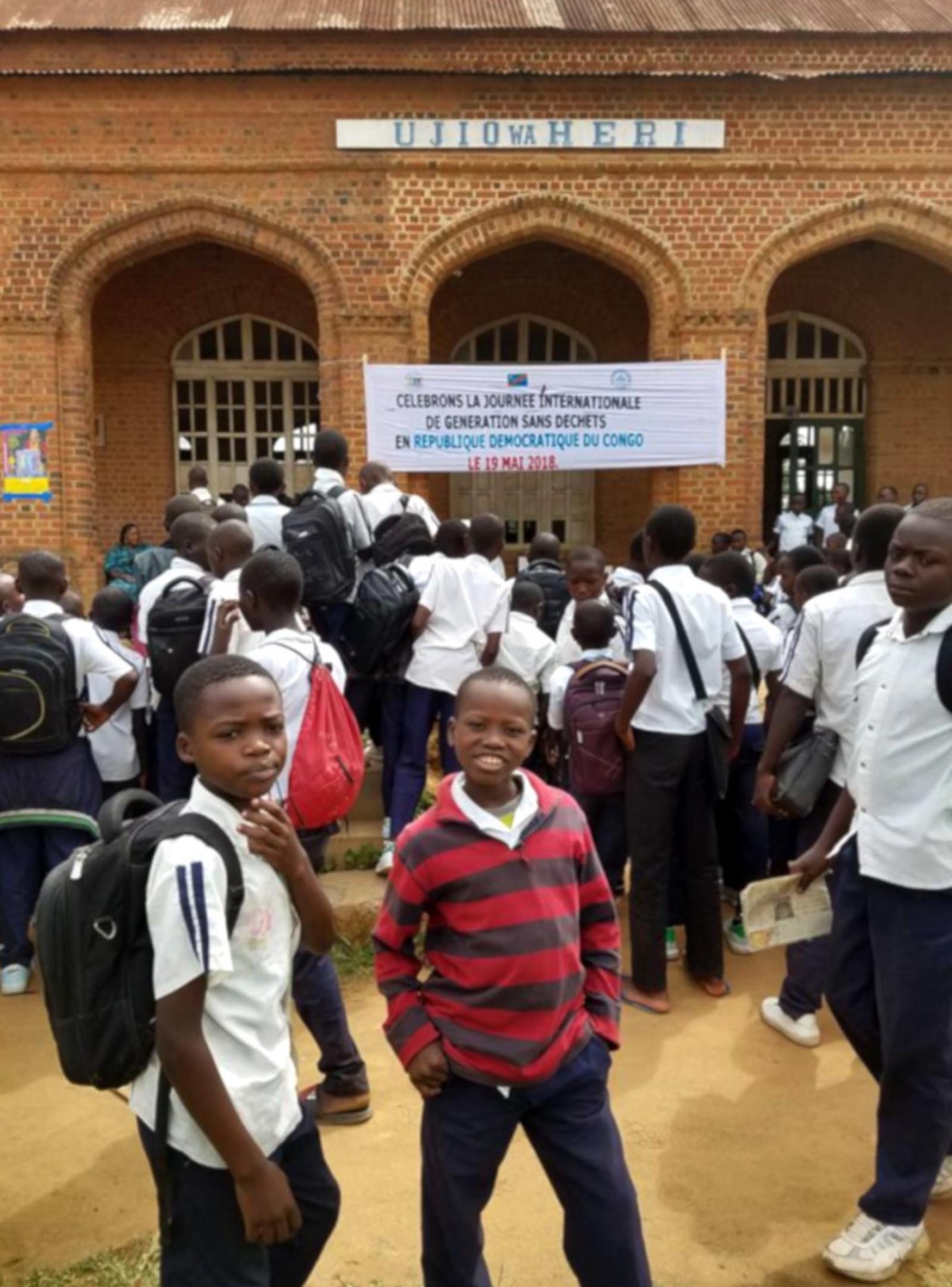 Two boys standing in front of the Ujio wa Heri institute, with other children in the background