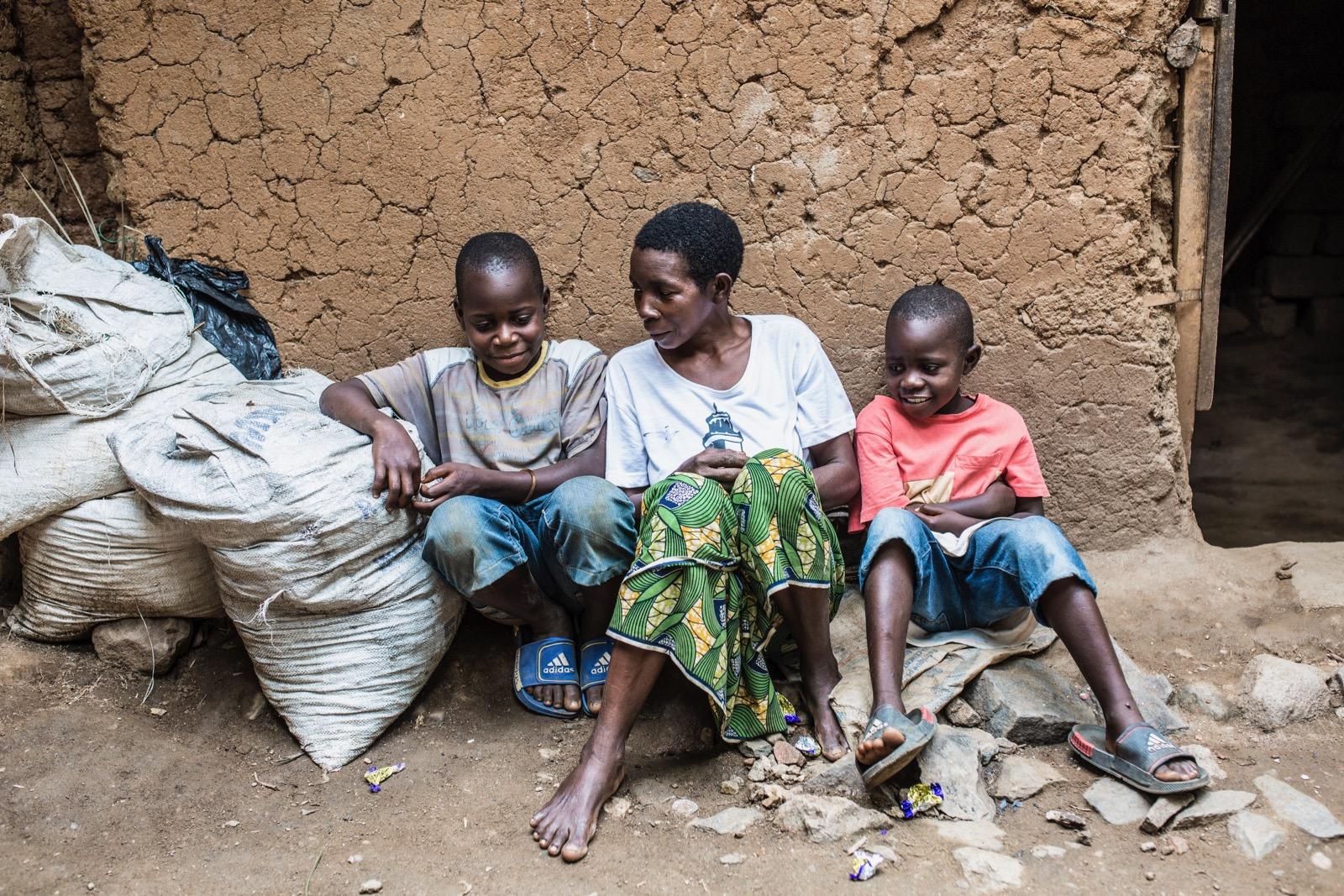Some children sitting on the ground, by a wall.