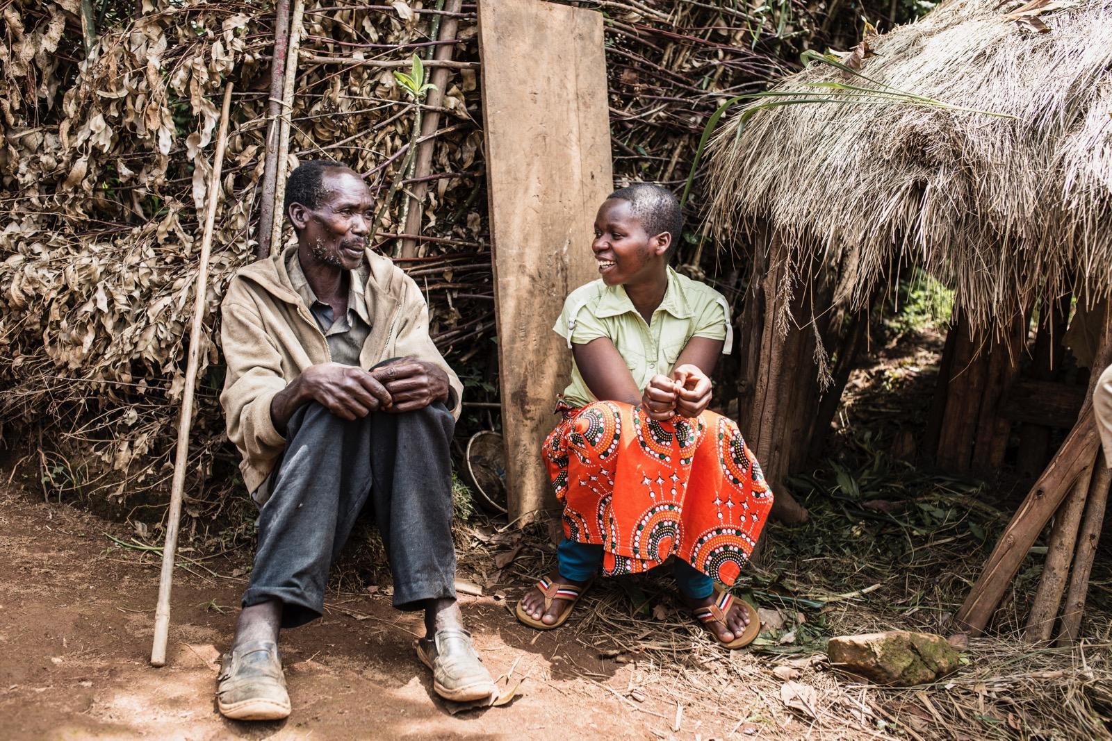 Two people sitting down on the ground, laughing with each other. 