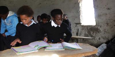 Two boys sitting in mud school classroom reading