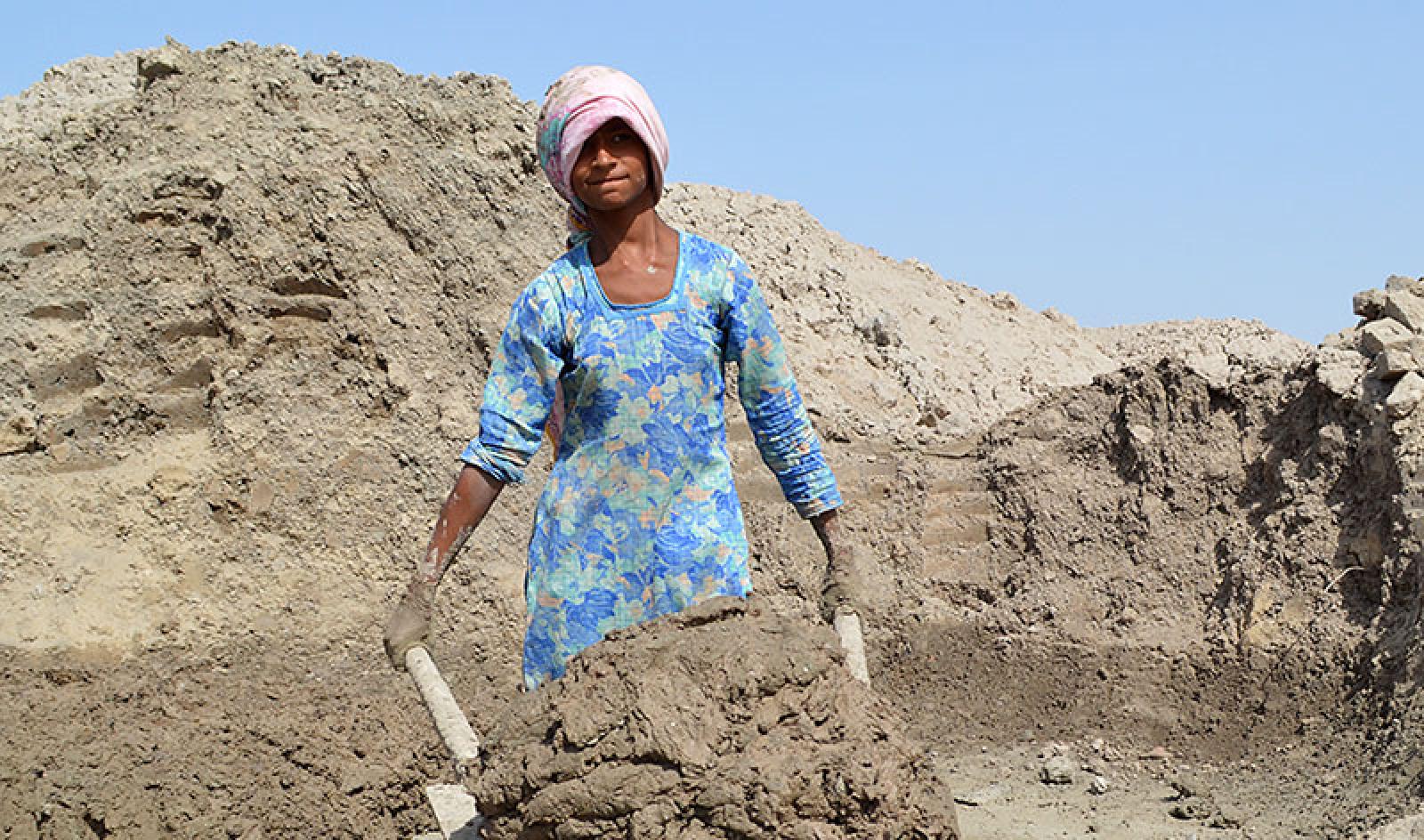 Afsana carts a clay mixture in a wheelbarrow. 