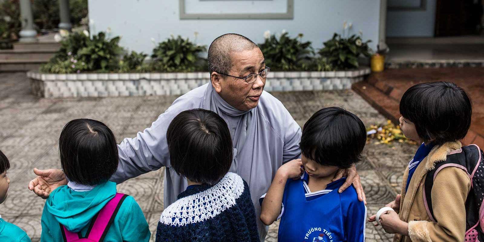 A buddhist nun has her arms around three children. 