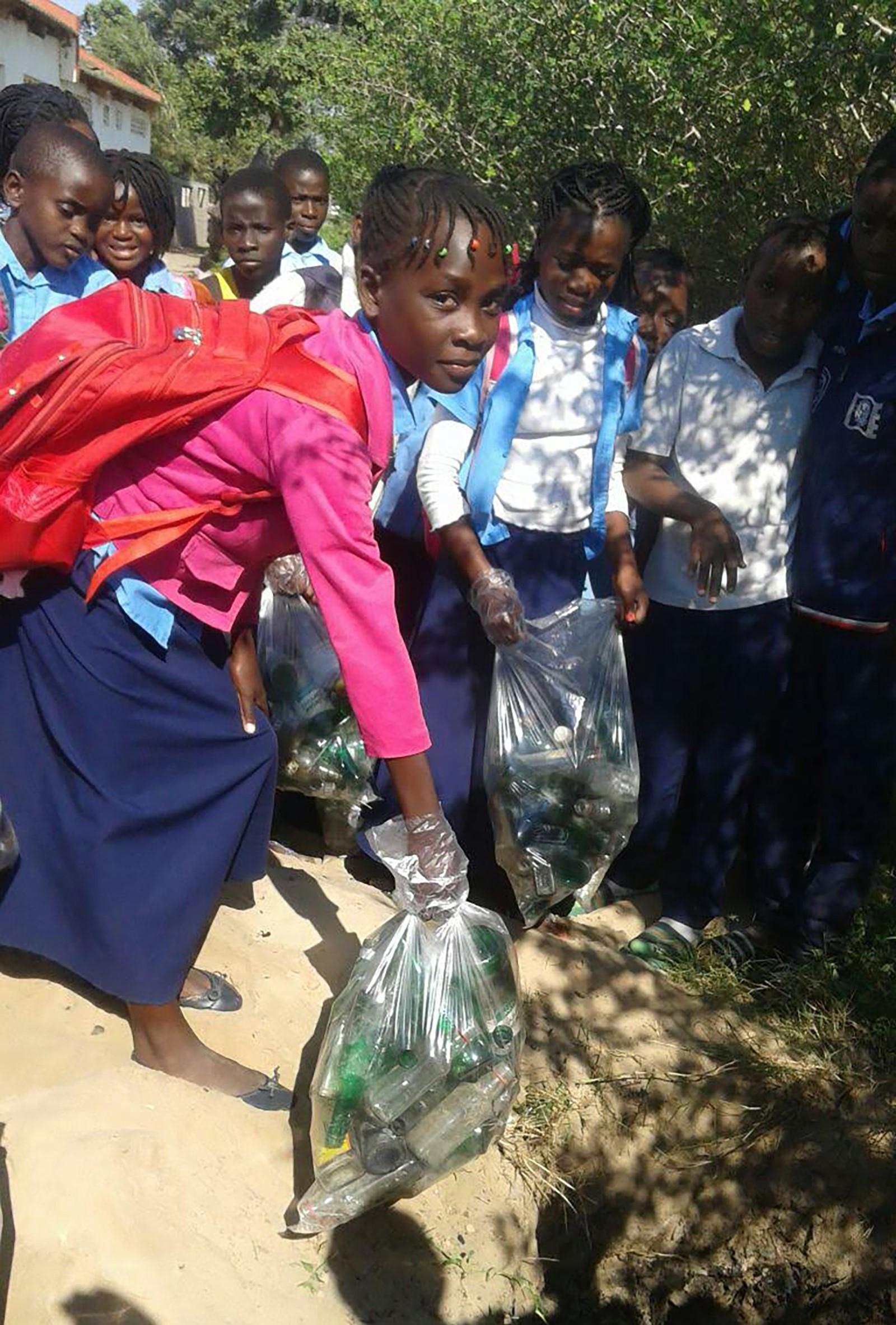 Girl with red backpack and pink shirt looking into the camera, holding a trash bag