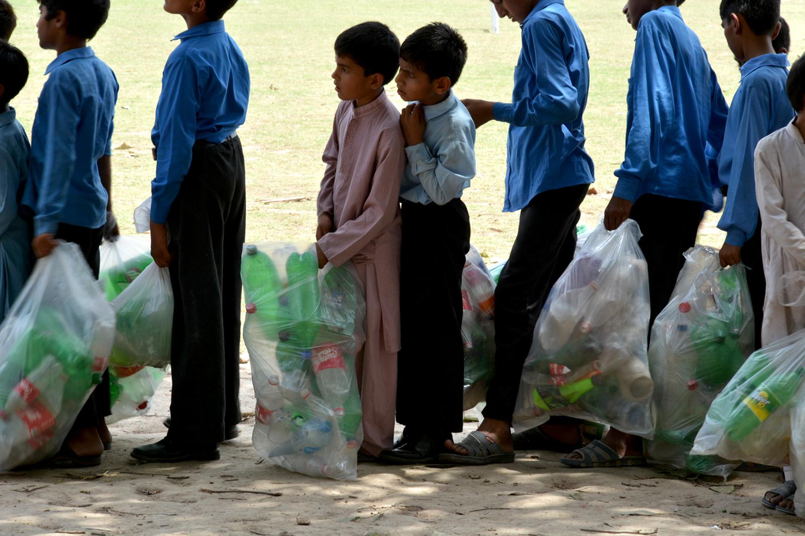 Two small boys in profile, standing close to each other in a line with other children