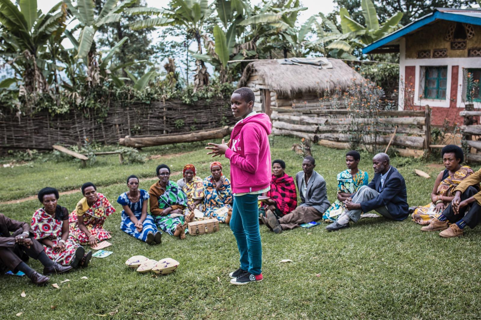 A young person standing in front of a group of people who are sitting down.