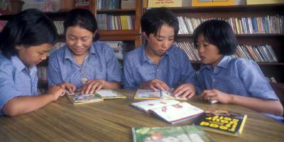 Four children in a library reading books together.
