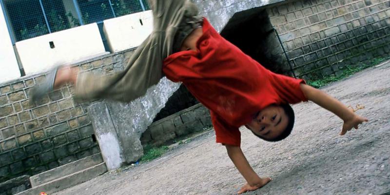 Small boy in red shirt and khaki pants does cartwheel.